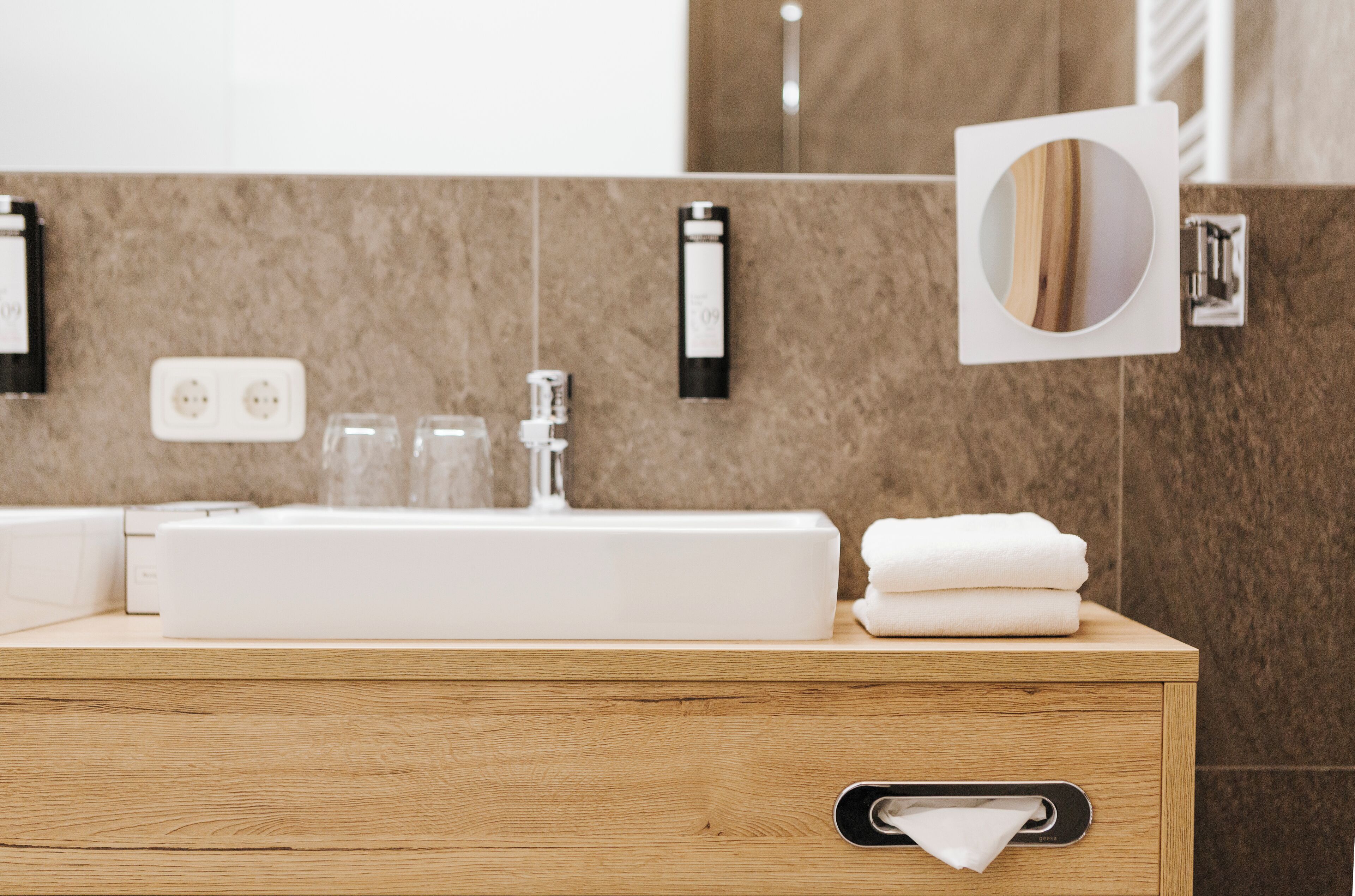 Un baño moderno con tocador de madera, un lavamanos blanco y un espejo.