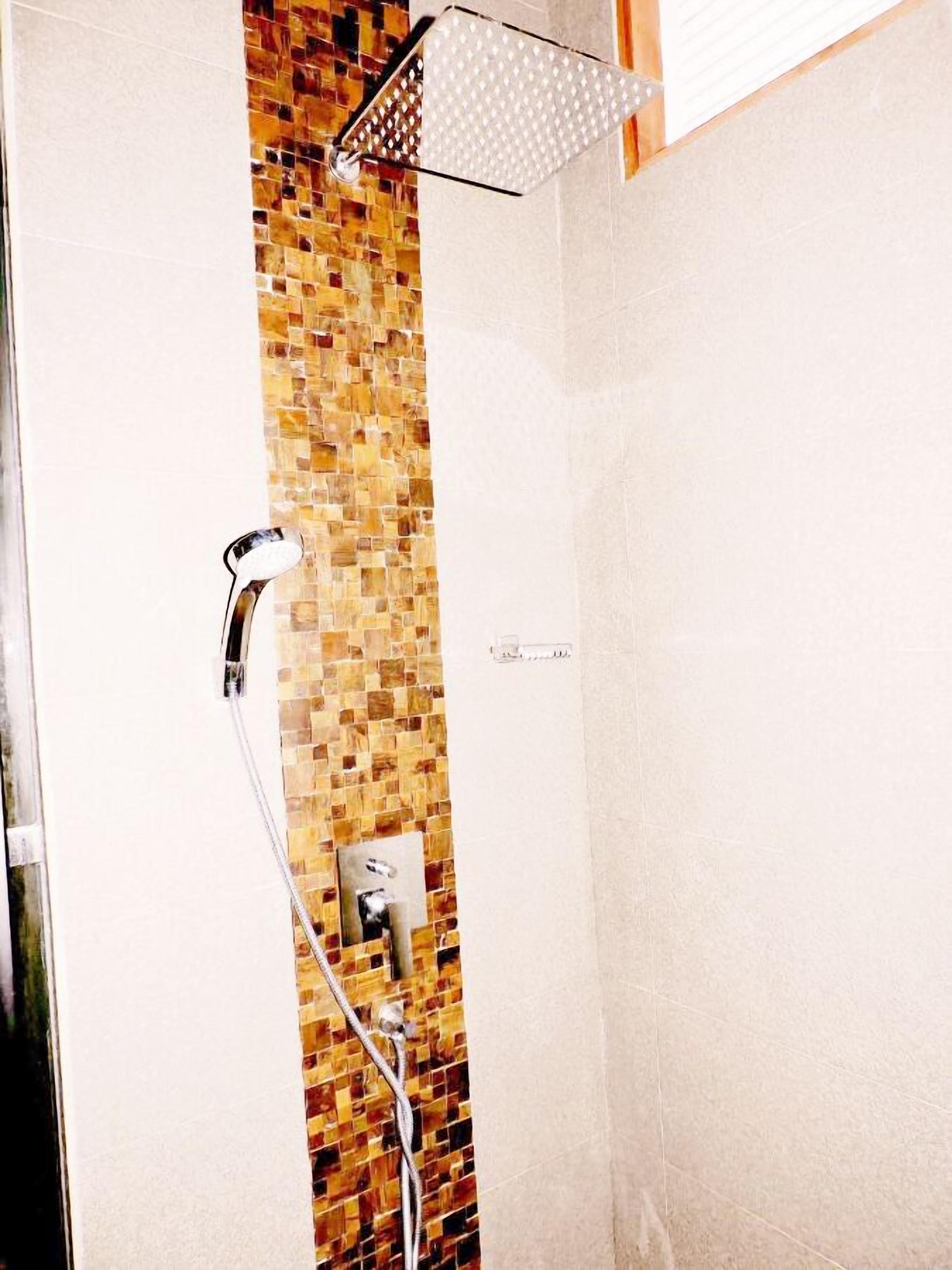 A shower with a mosaic tile wall and a handheld showerhead.