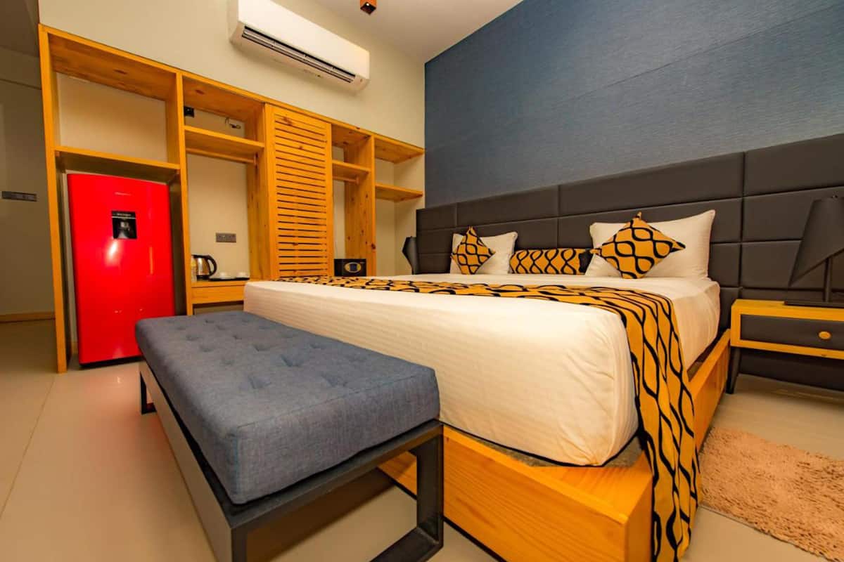 Une chambre avec un lit, un banc, un réfrigérateur rouge et des étagères en bois intégrées.