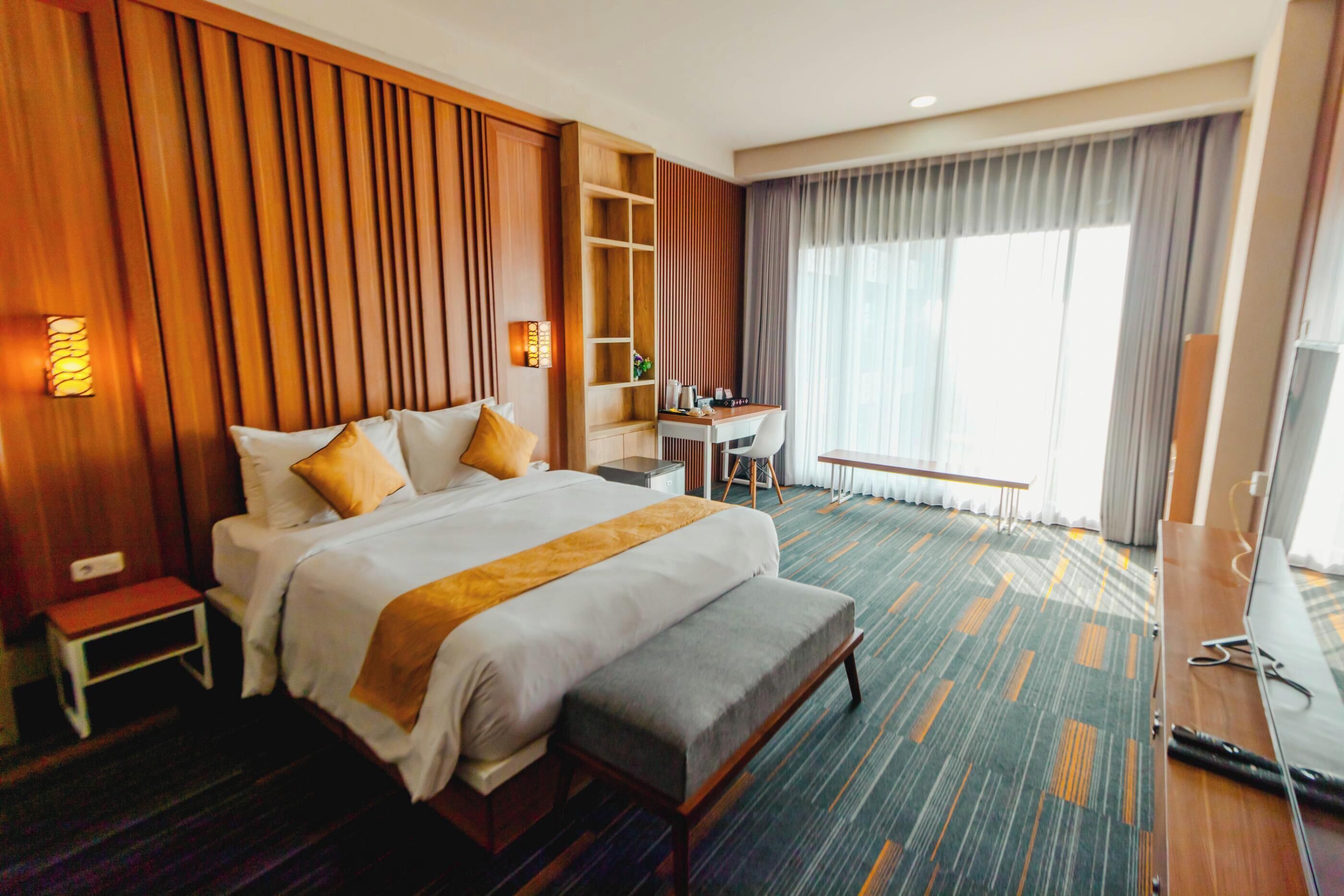 A hotel room with a large bed, a desk, a chair, a small table, and a bench.
