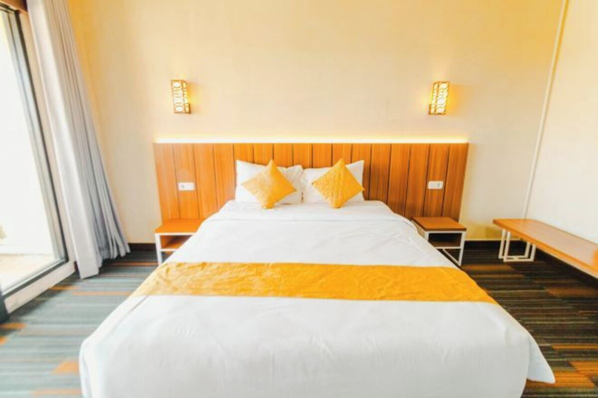 A hotel room with a large bed, wooden headboard, bedside tables, and a bench.