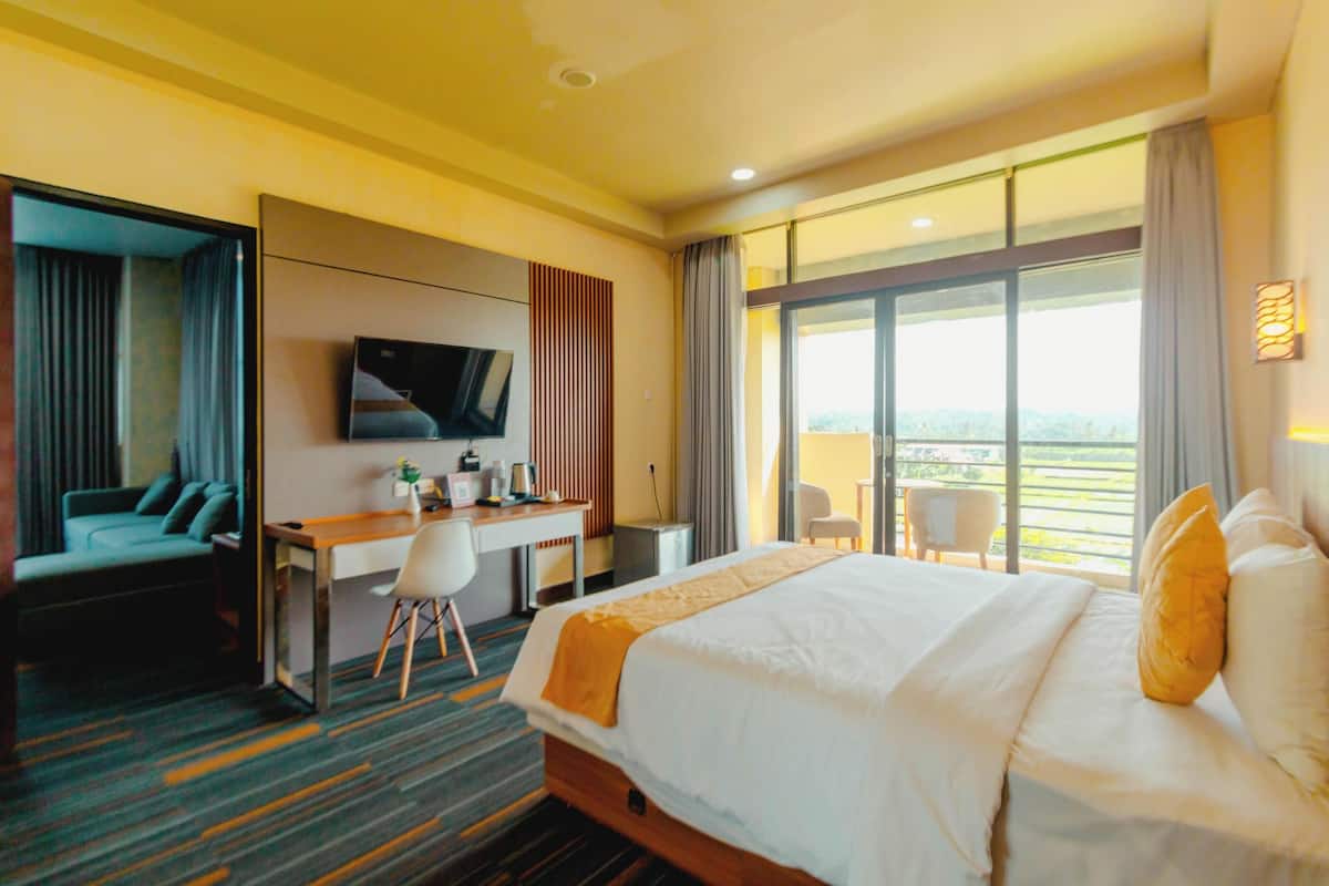 A hotel room with a large bed, a desk with a chair, a TV mounted on the wall, and a balcony with a view.