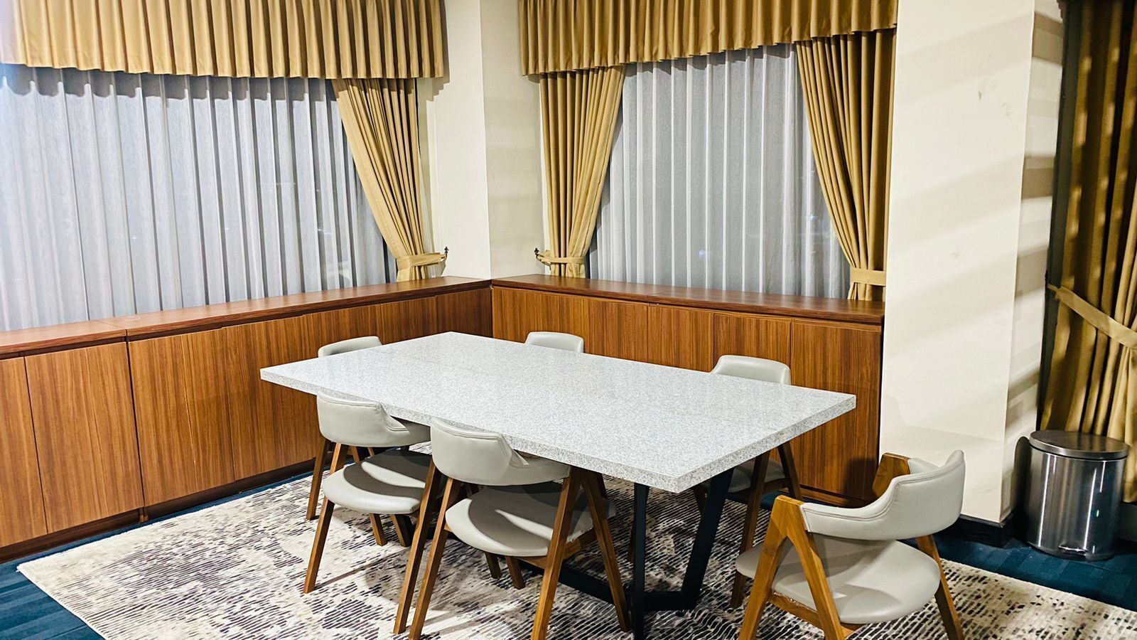 Uma sala de conferências com uma mesa retangular e seis cadeiras, painéis de madeira nas paredes e um tapete estampado no chão.