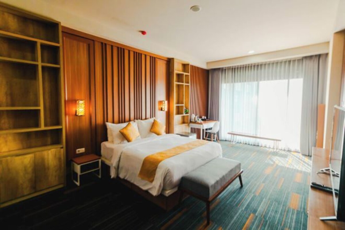 Habitación de hotel con una cama grande, un escritorio, una silla y un ventanal con cortinas.