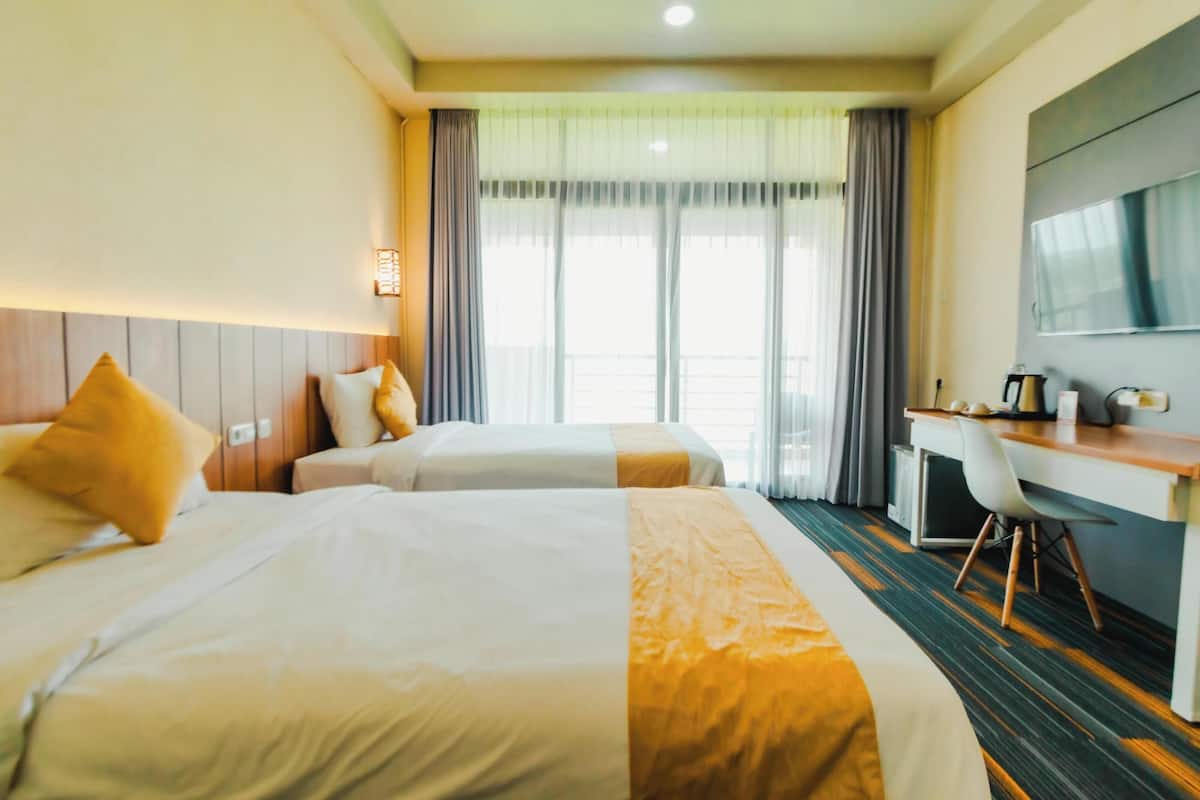 A hotel room with two beds, a desk, a chair, and a large window with curtains.