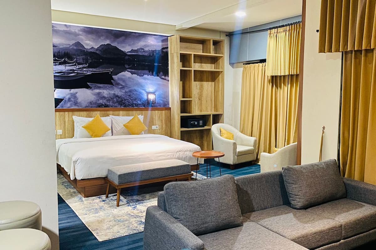 A hotel room with a large bed, a sofa, a small table, and a wall-mounted TV.
