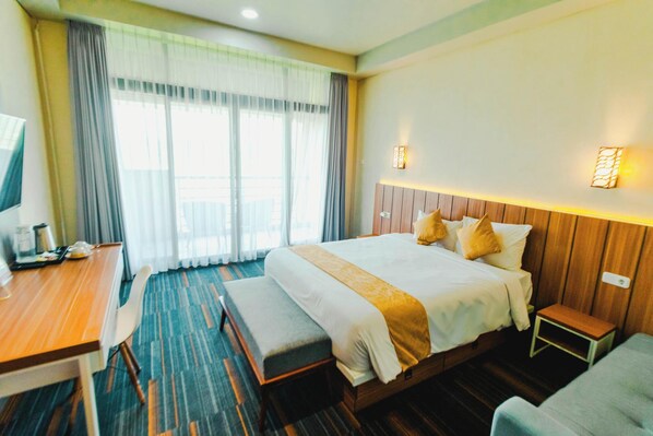 A hotel room with a large bed, a desk with a chair, a small table, and a bench. - De Balen Soultan Hotel (Jonggat)