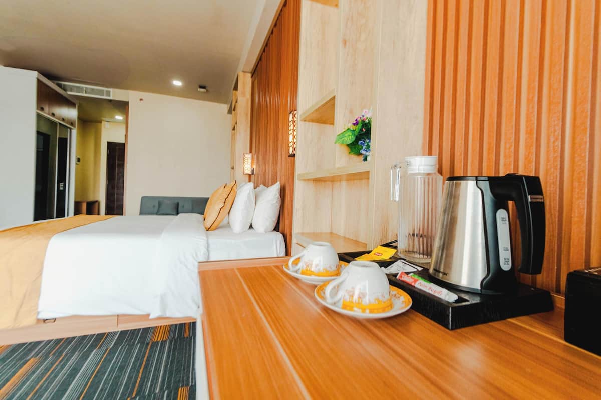 A hotel room with a bed, a wooden table with a coffee maker, cups, and a small plant.