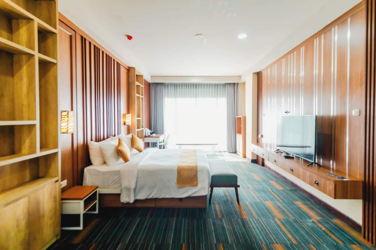 A hotel room with a large bed, a TV, a desk, and a wardrobe.
