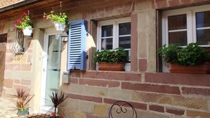 Un edificio de dos pisos con fachada de piedra, techo de tejas y un pequeño patio con mesa y sillas.