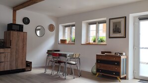 Una cocina con armarios de madera, una mesa de comedor con sillas, un microondas y un reloj en la pared.