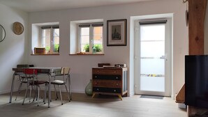 Una sala de estar con una mesa de comedor, sillas, un televisor, un mueble de madera y un ventanal con vistas a zonas verdes.