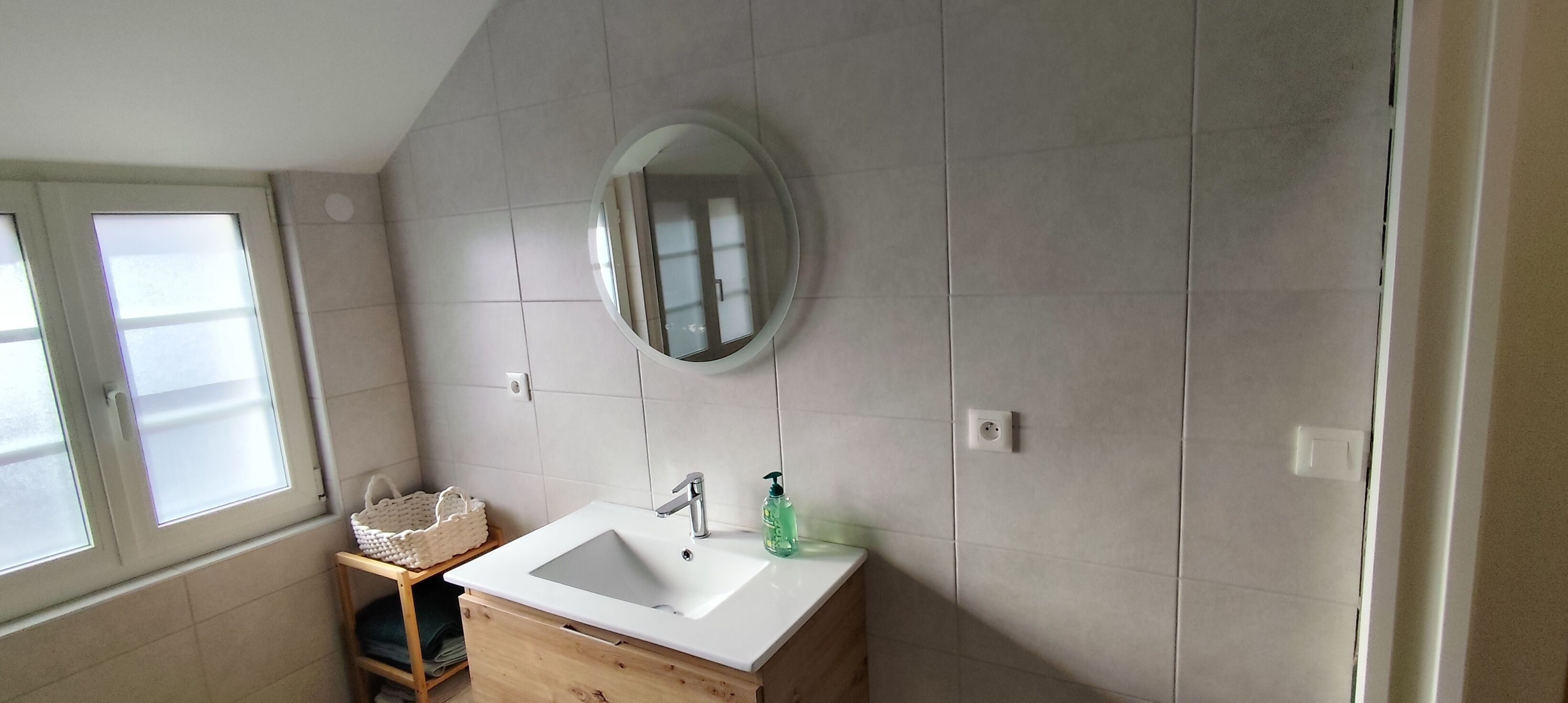 A bathroom with a white sink, a round mirror, and a wooden vanity.