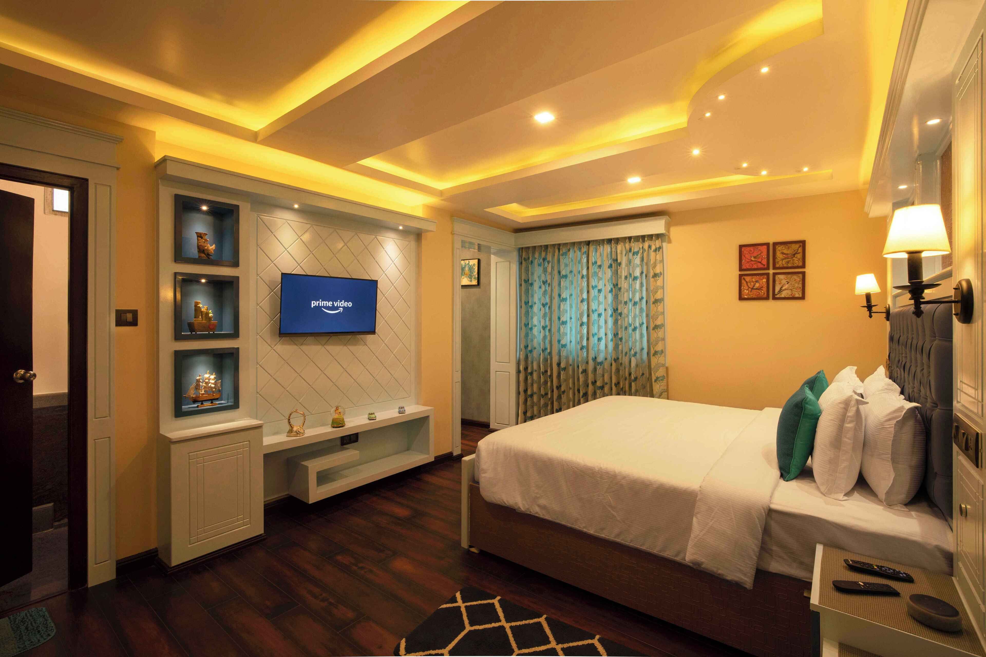 Une chambre d’hôtel moderne avec un grand lit, un téléviseur fixé au mur, une coiffeuse avec des étagères et une fenêtre avec des rideaux.