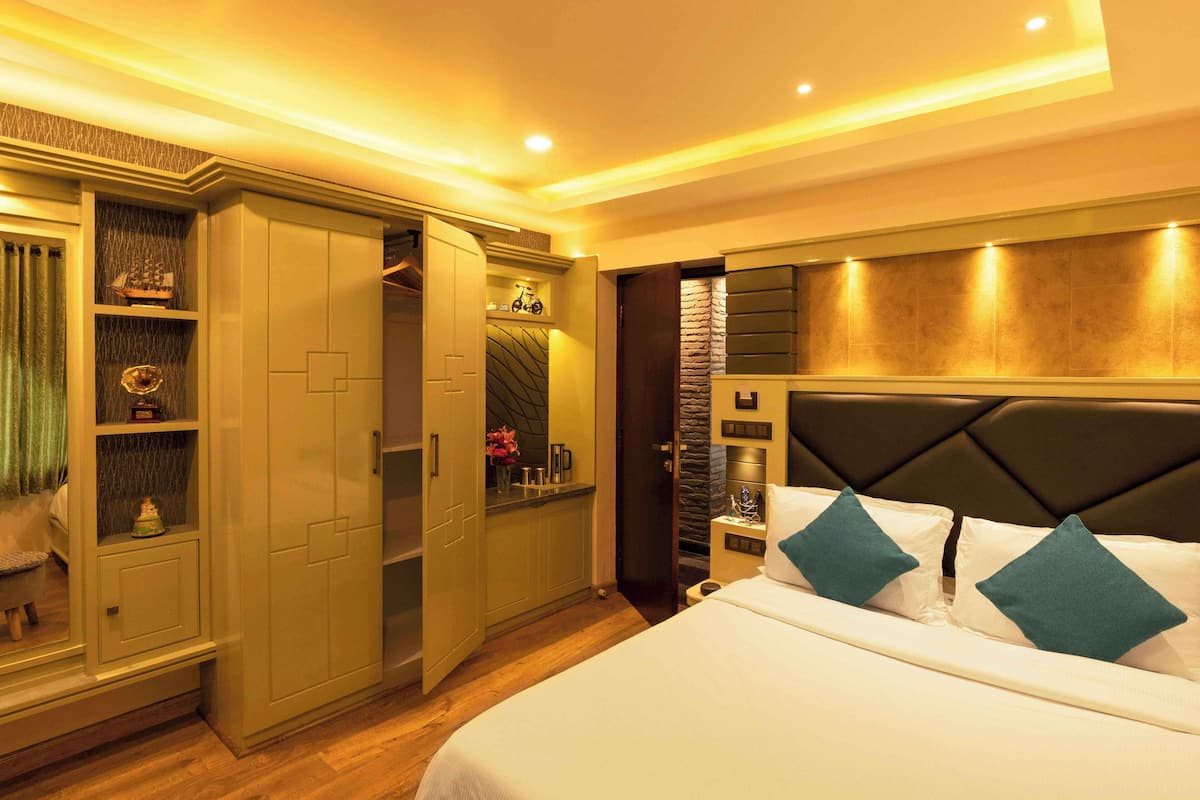 Quarto de hotel com uma cama, um guarda-roupa, uma penteadeira com espelho e um pequeno espaço de estar.