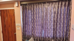 A room with a blue sofa, patterned curtains, a wooden door, and tiled flooring. - HERITAGE VIEW (Ootacamund)