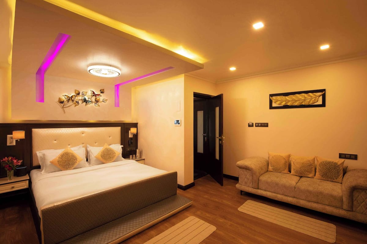Quarto de hotel moderno com cama grande, sofá e luminária decorativa no teto.