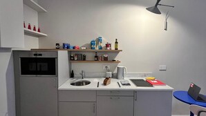 A compact kitchen with a built-in oven, a sink, and a small dining area with a laptop and chair. - Design micro apartment in the Porta Venezia Design District (Milano)