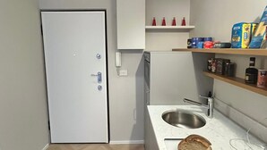 A compact kitchen with a built-in refrigerator, a sink, and a small countertop. There are shelves above the sink with various food items and a loaf of bread on the counter. - Design micro apartment in the Porta Venezia Design District (Milano)