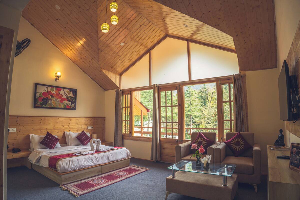 A bedroom with a large bed, a sofa, a coffee table, and a window with a view of trees.