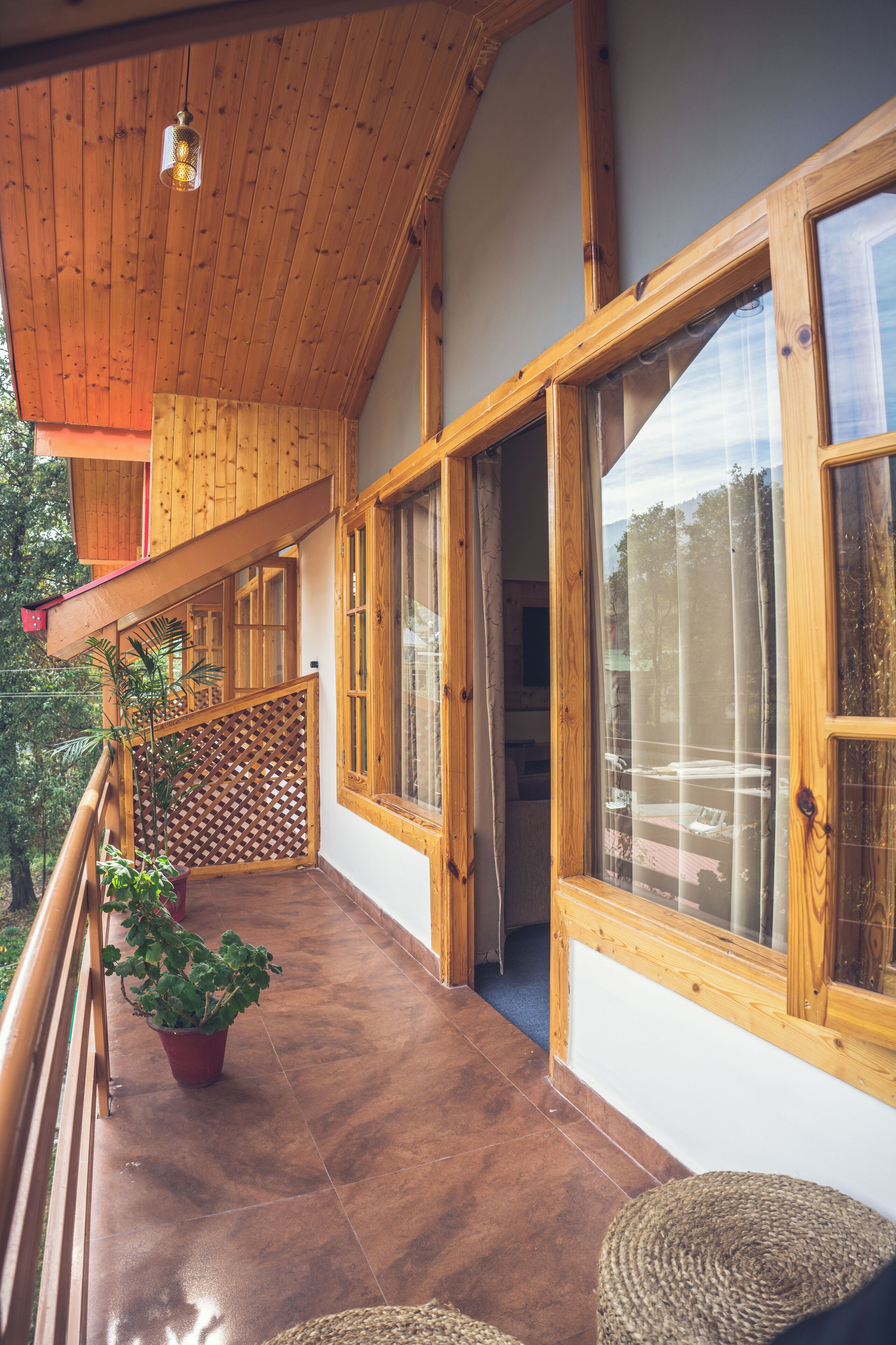 Un balcón de madera con macetas, un banco tejido y vistas al exterior.