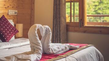 Un lit recouvert d’une couverture rouge et blanche, avec une tête de lit en bois et une fenêtre donnant sur les montagnes.
