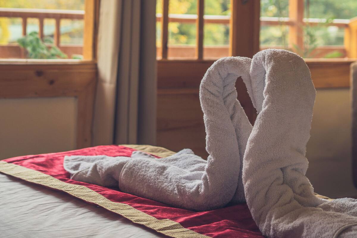 A room with a bed, a window with a view of mountains, and a wooden railing.