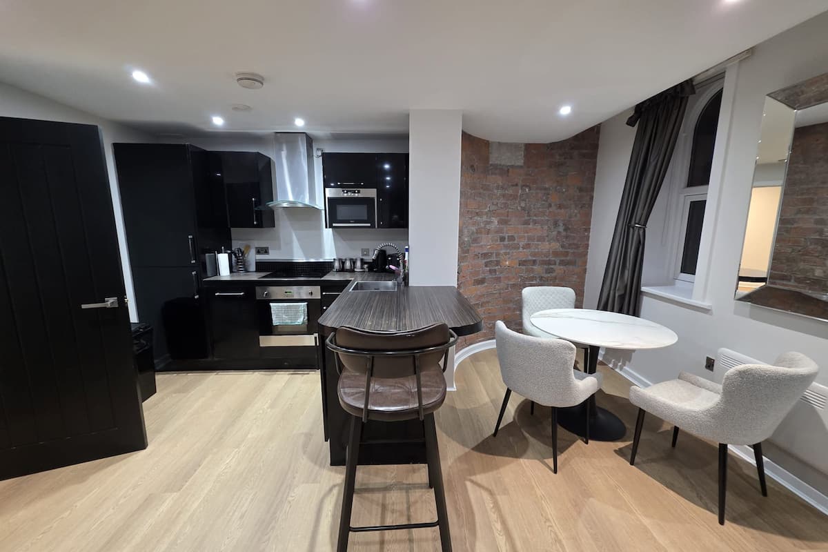 A modern kitchen with black cabinetry, a central island, and a dining area with two chairs and a small table.