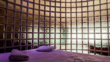 A room with a curved glass partition, a bed with a purple bedspread, and a towel on the bed.
