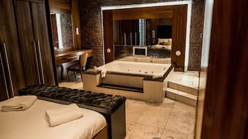 Un dormitorio moderno con una cama grande, una zona de estar separada, una bañera y un tocador con espejo.