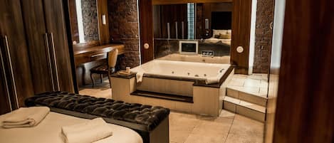 A modern bedroom with a large bed, a separate seating area, a bathtub, and a vanity with a mirror.
