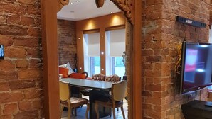 A dining area with a brick wall, a wooden archway, a dining table with chairs, and a television mounted on the wall. - Infinity Partypadsliverpool Hen and Stag Welcome (Liverpool)