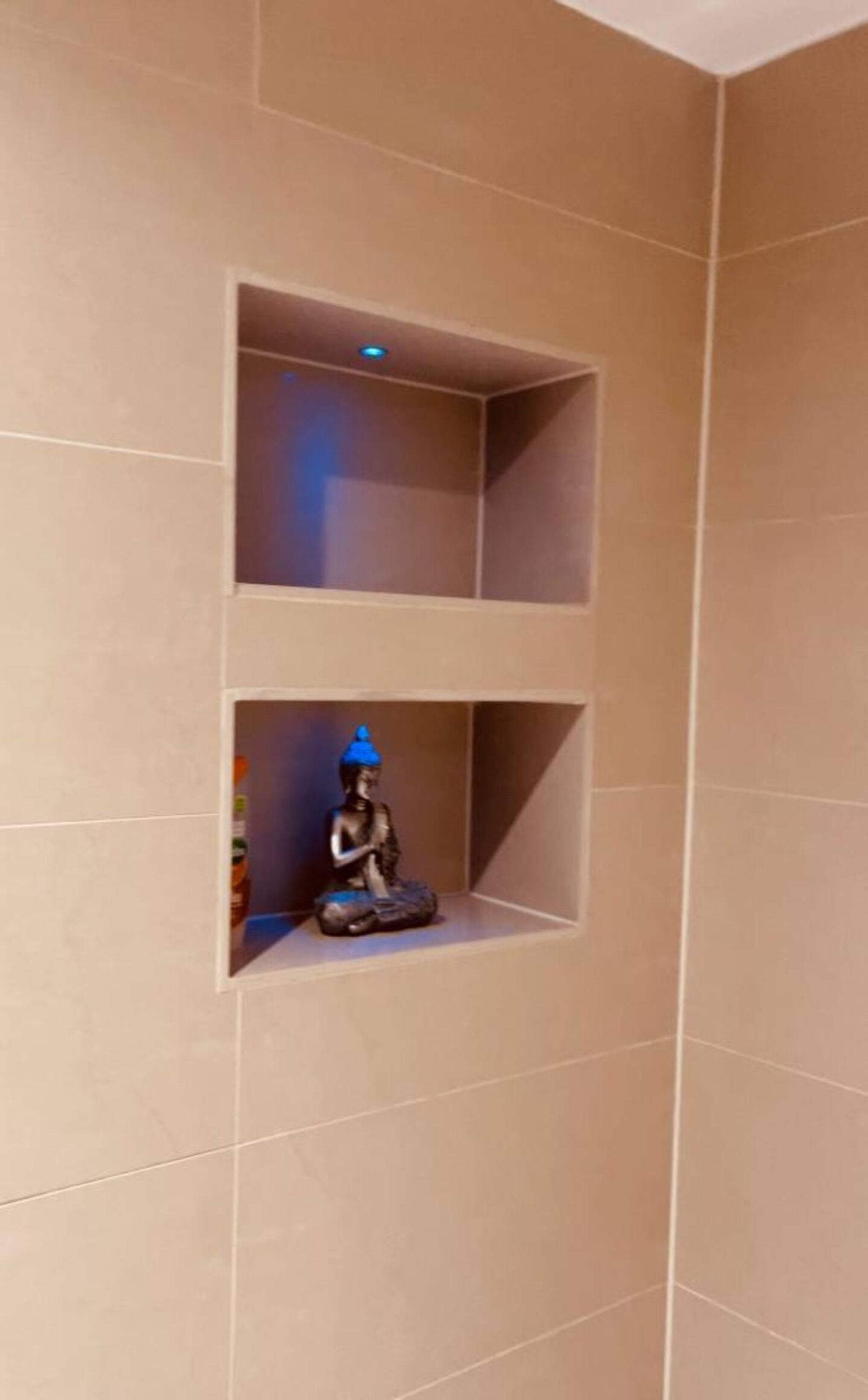 A corner of a room with beige tiled walls and two empty shelves.