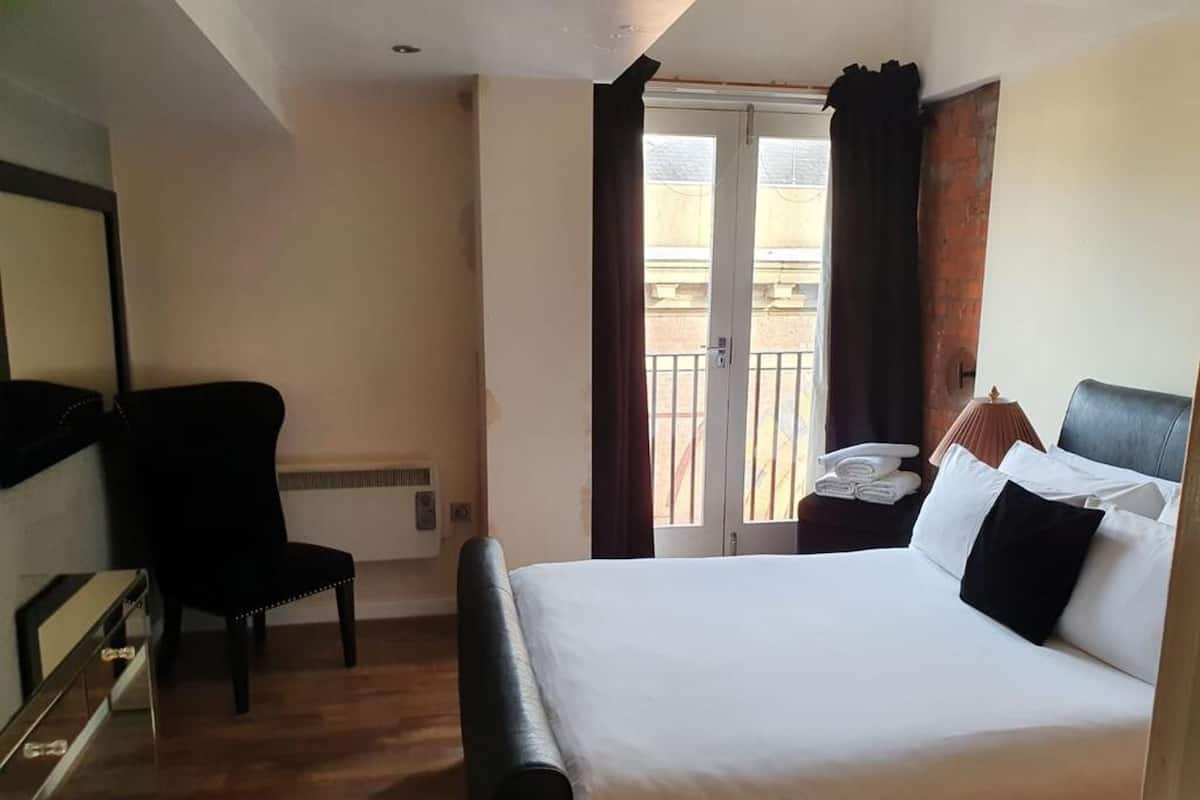 A hotel room with a bed, a chair, a desk, a lamp, and a window with curtains.