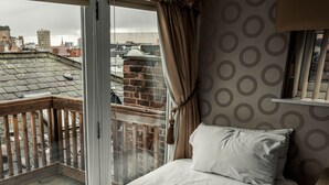 A room with a large window overlooking a cityscape, a bed with white bedding, and a patterned wall. - Infinity Partypadsliverpool Hen and Stag Welcome (Liverpool)