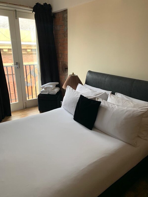 Une chambre d’hôtel avec un grand lit, une table de chevet avec une lampe, un téléphone et une vue sur le balcon extérieur.