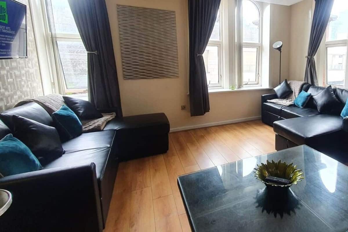 A modern living room with leather sofas, a glass coffee table, and a large window with curtains.
