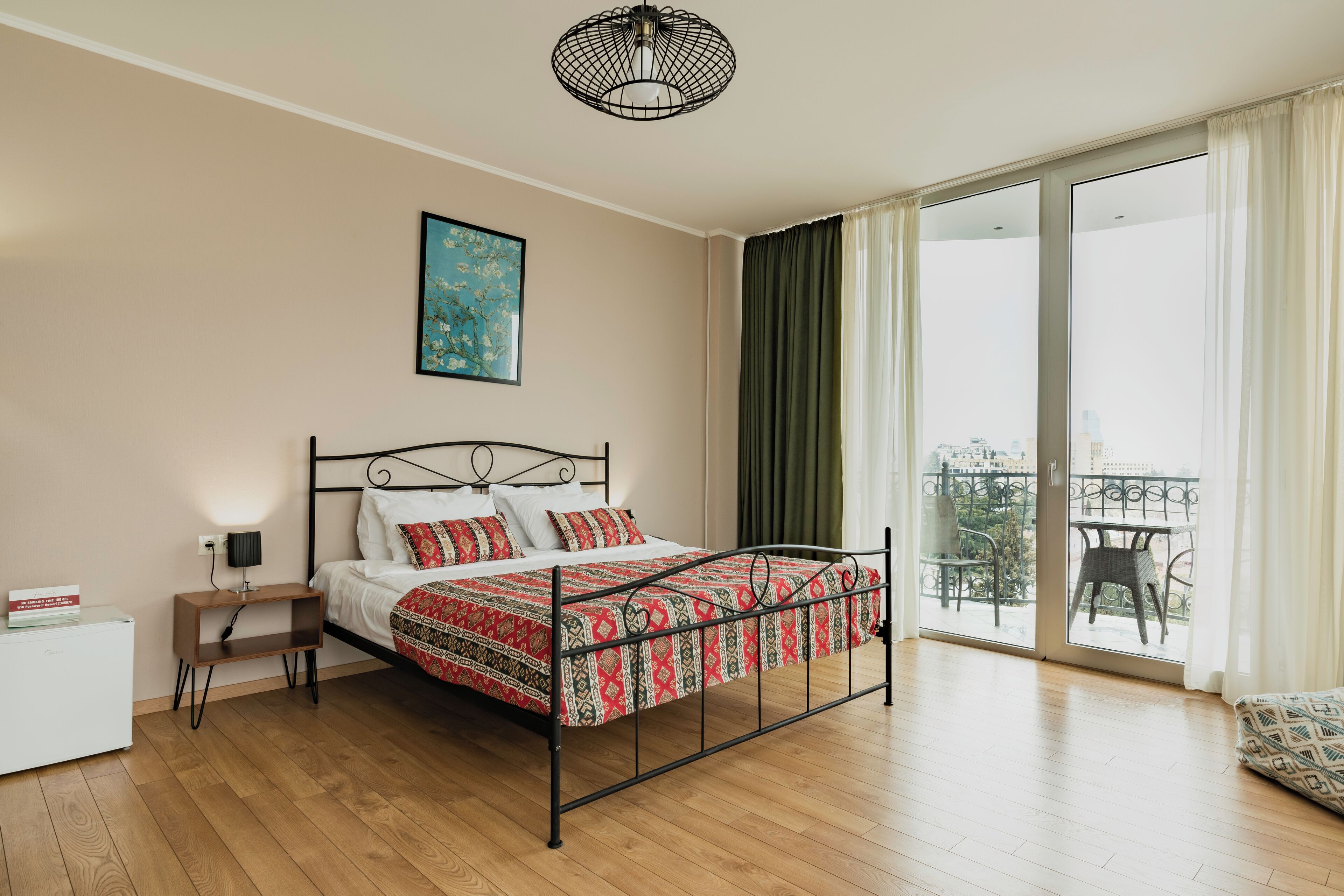 A bedroom with a bed, a bedside table, a nightstand, a window with curtains, and a view of the outside.