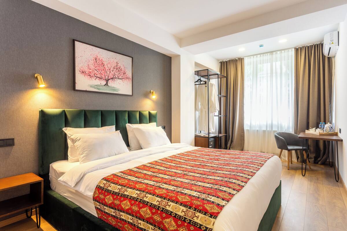 Une chambre d’hôtel avec un grand lit, un bureau avec une chaise, une armoire et une fenêtre avec des rideaux.