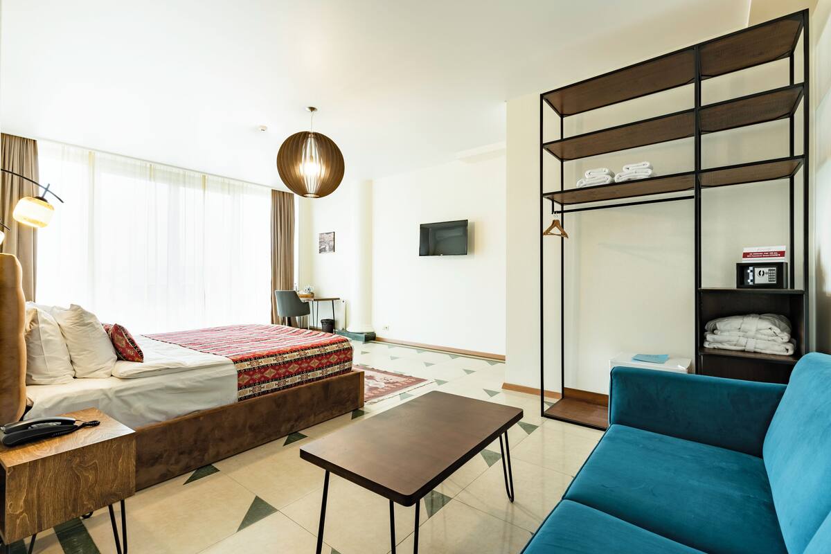 Une chambre d’hôtel moderne avec un lit, un canapé bleu, une petite table, une armoire et un téléviseur fixé au mur.