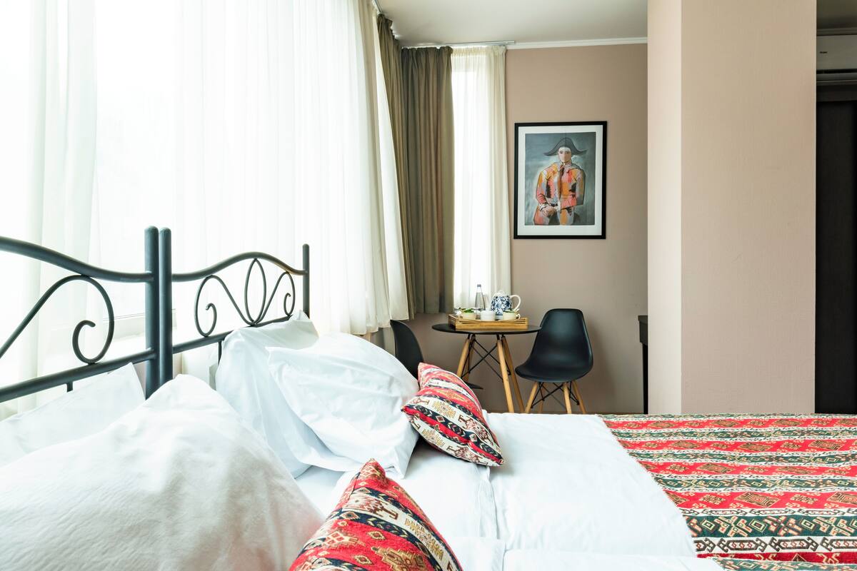 Une chambre d’hôtel avec un lit, des oreillers, une table avec une théière et une chaise.