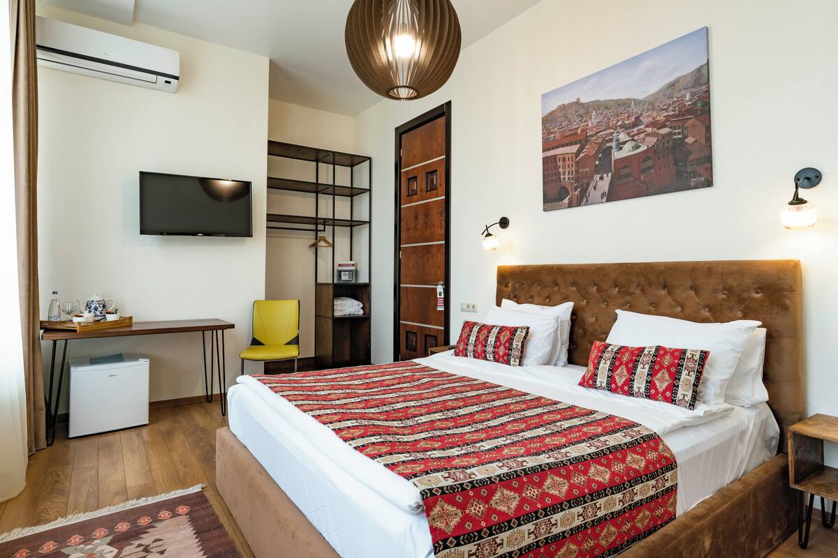 Une chambre d’hôtel avec un grand lit, un bureau avec un ordinateur, une chaise, une armoire et un téléviseur fixé au mur.