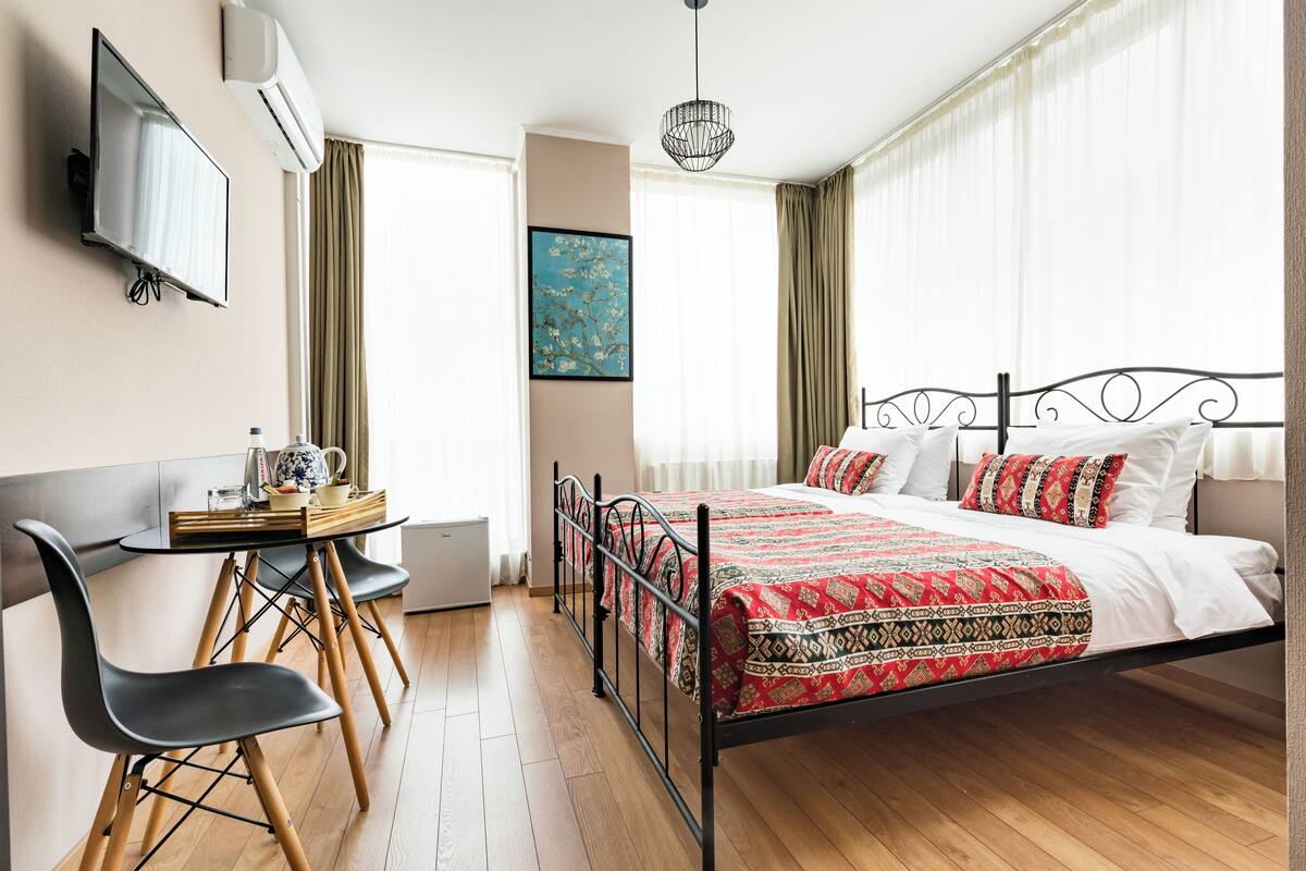 Une chambre d’hôtel avec un lit, un bureau avec des chaises, une télévision et un tableau au mur.
