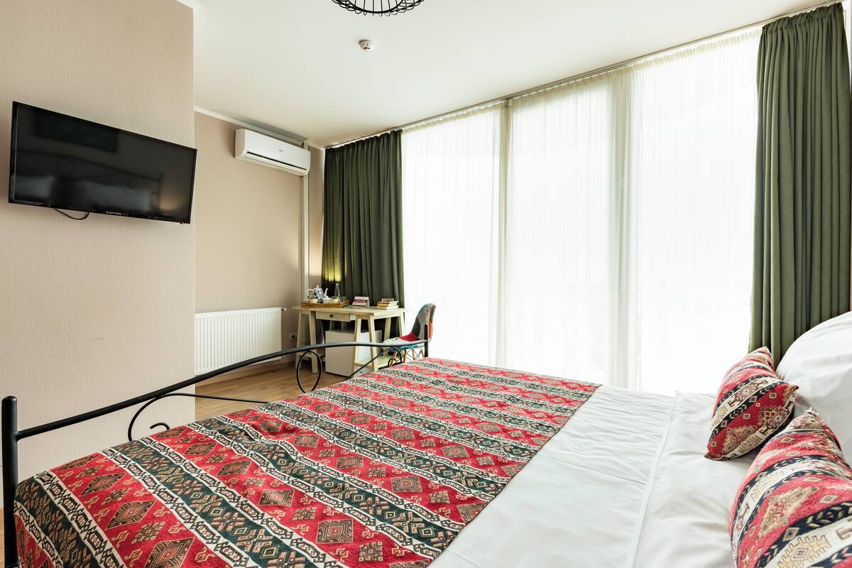 Une chambre d’hôtel équipée d’un lit, d’un bureau, d’une chaise, d’une télévision et d’une fenêtre avec des rideaux.