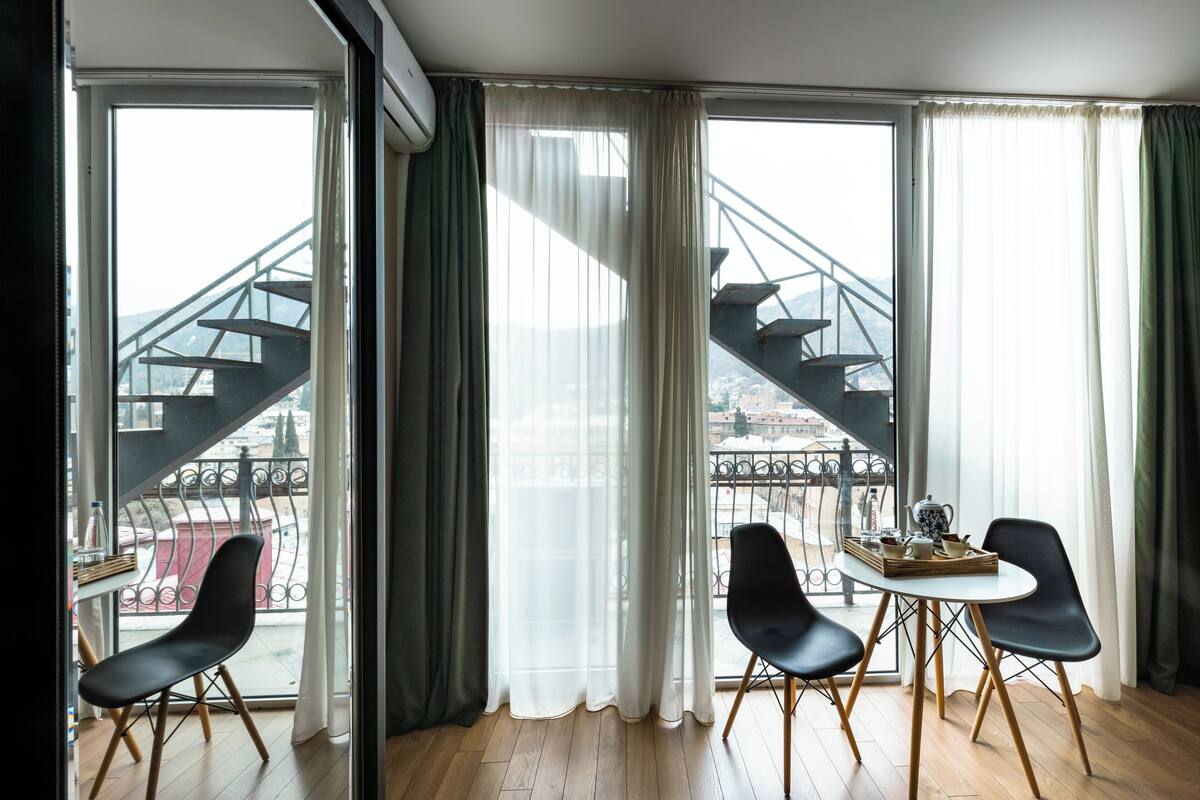 Une chambre avec un balcon, une table avec des chaises et une vue sur un escalier extérieur.