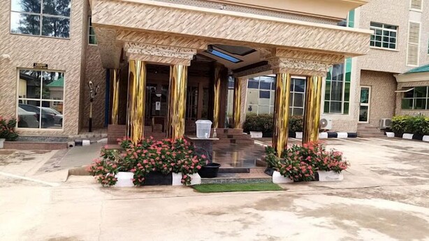 A building with a covered entrance, steps leading up to it, and potted plants with pink flowers. - Trophy Hotel LTD (Kaduna)