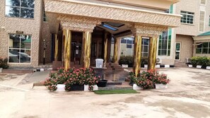 A building with a covered entrance, steps leading up to it, and potted plants with pink flowers. - Trophy Hotel LTD (Kaduna)