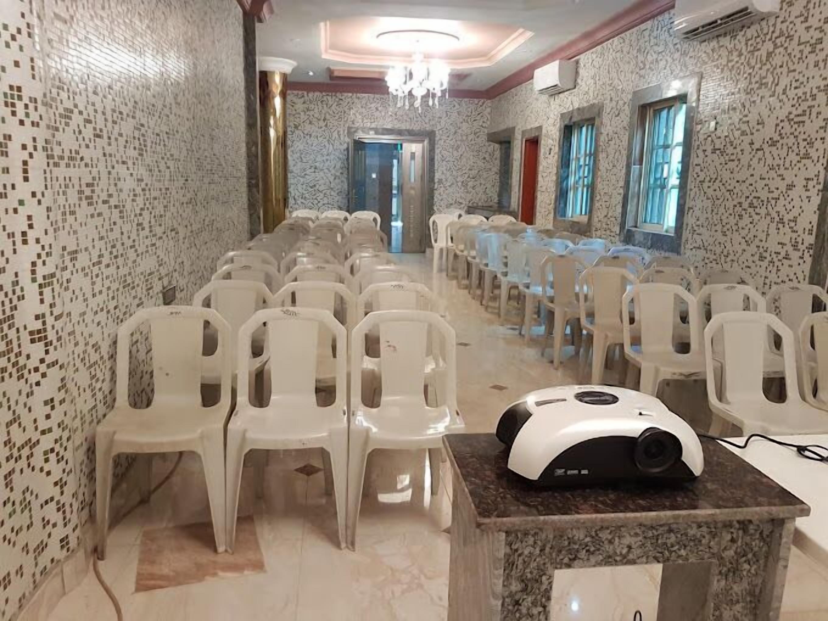 A conference room with rows of white plastic chairs, a projector on a marble table, and patterned walls.