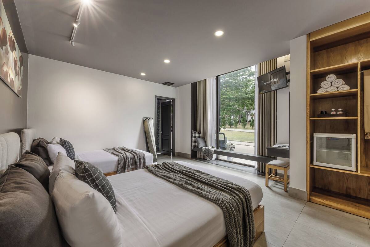 A modern hotel room with a large bed, a seating area with a view, and a wooden shelf with toiletries.