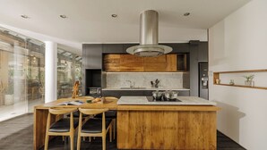 A modern kitchen with a central island, wooden chairs, a built-in microwave, and a stainless steel range hood. - The K'rin Villa (Xuan Huong - Da Lat)